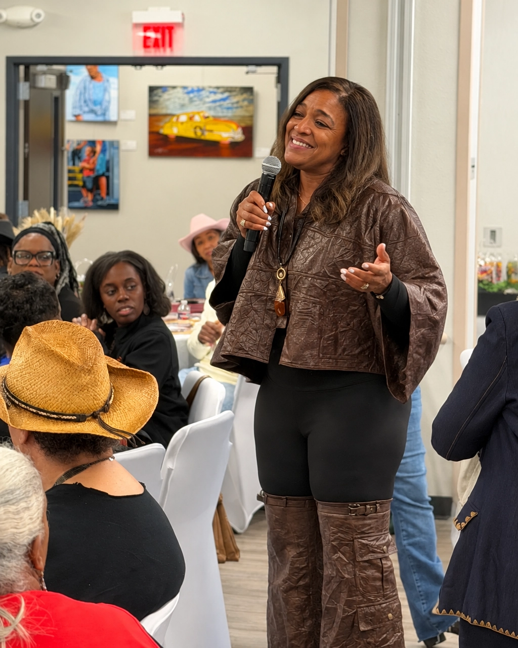 Leah smiling while holding a microphone in her brown outfit, with conference attendees in the background